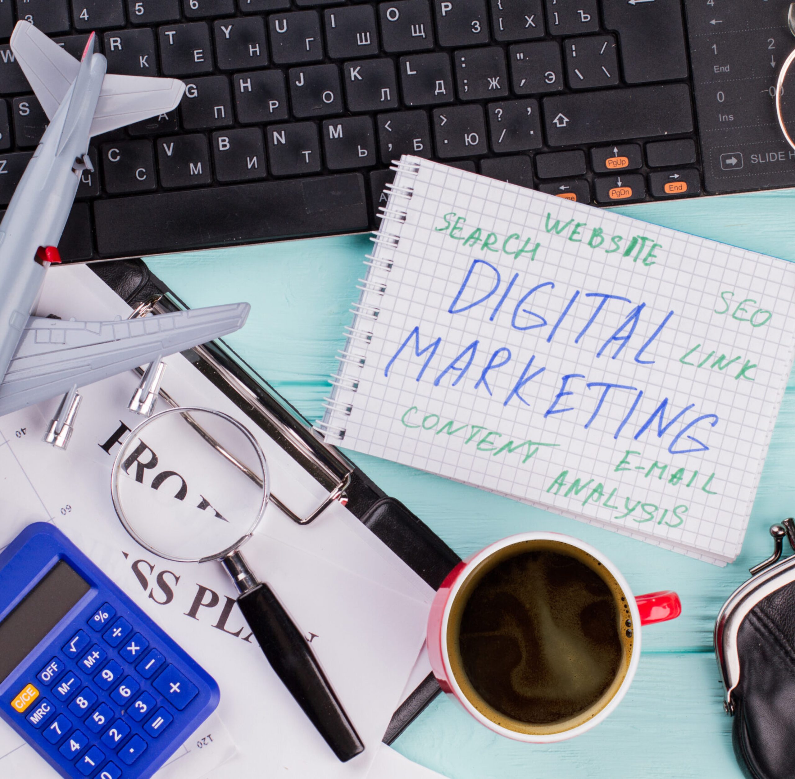 Digital marketing on notepad and various office supplies. Flat lay composition with keyboard, coffee and other office related objects on blue background.